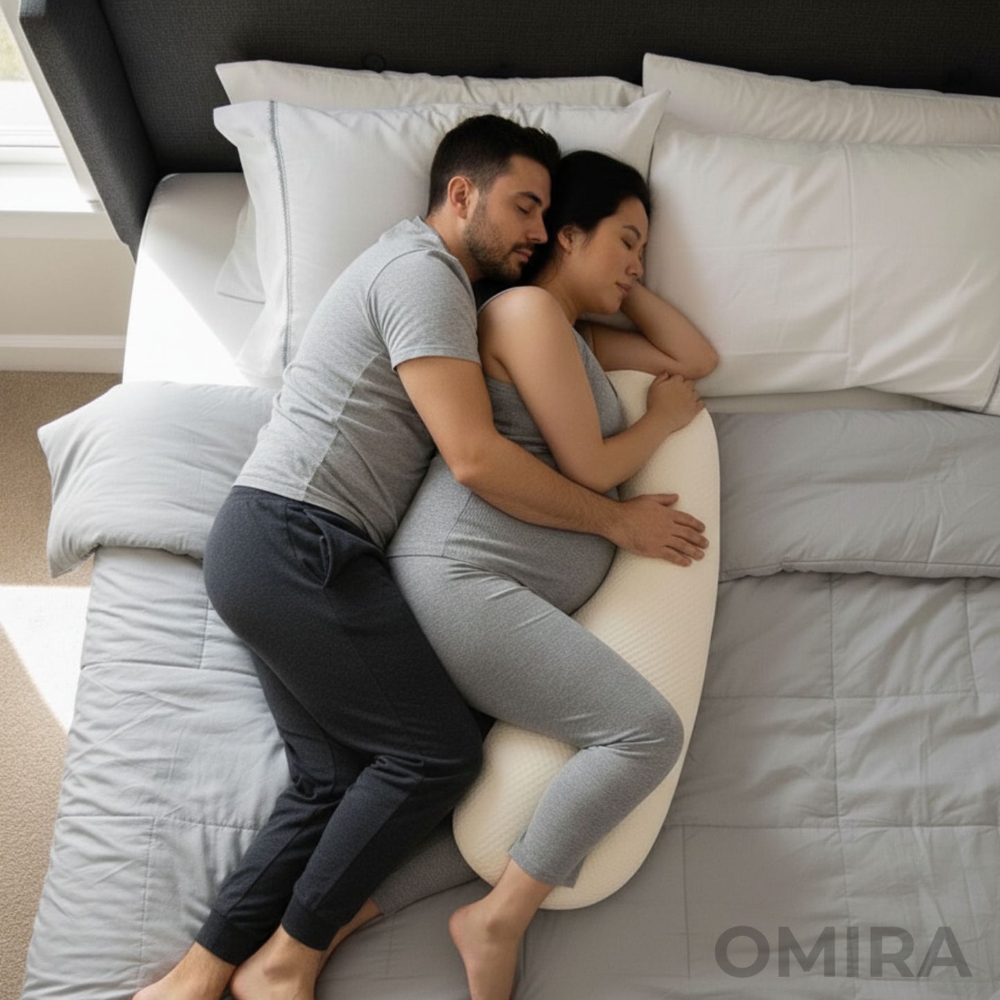 Couple lying on a bed with a slim white pregnancy pillow that supports comfort and closeness.
